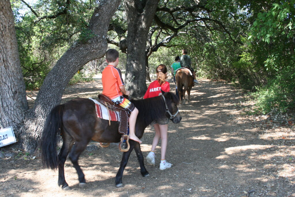 Counselor leading a child on a pony ride through the trees